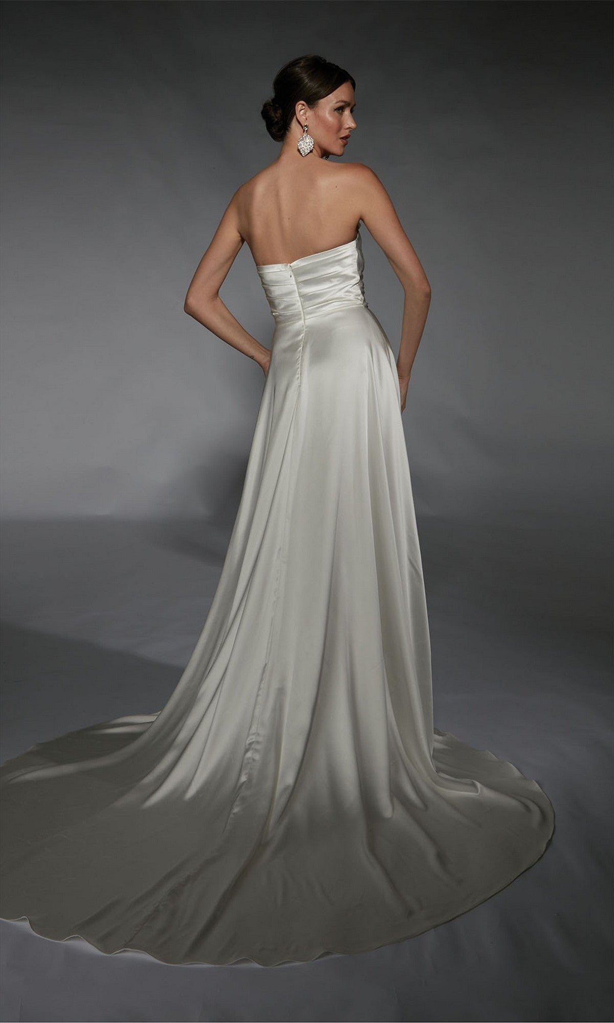 A woman in the Alyce 7107 long white strapless satin A-line dress with a train stands facing away against a plain gray backdrop.